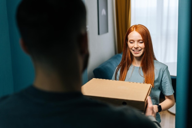 Jolie jeune femme heureuse recevant des boîtes en papier avec de la pizza chaude du livreur à la porte à la maison