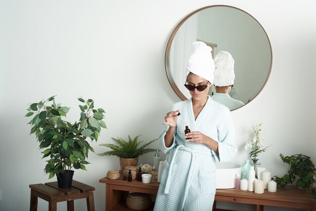 Une jolie jeune femme hydrate sa peau avec son sérum hylauron dans sa baignoire lumineuse