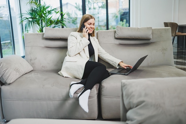 Jolie jeune femme indépendante en tenue décontractée se reposant sur un canapé tout en travaillant sur Internet via netbook tout en travaillant à distance sur un projet à la maison