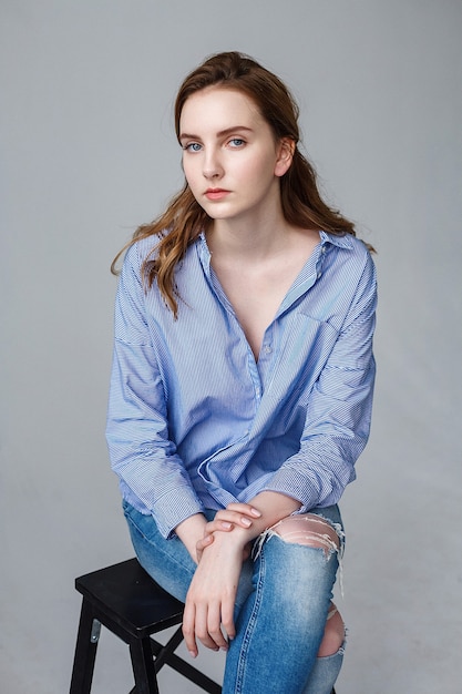 Jolie jeune femme jolie caucasienne aux cheveux longs en chemise bleue et jeans déchirés