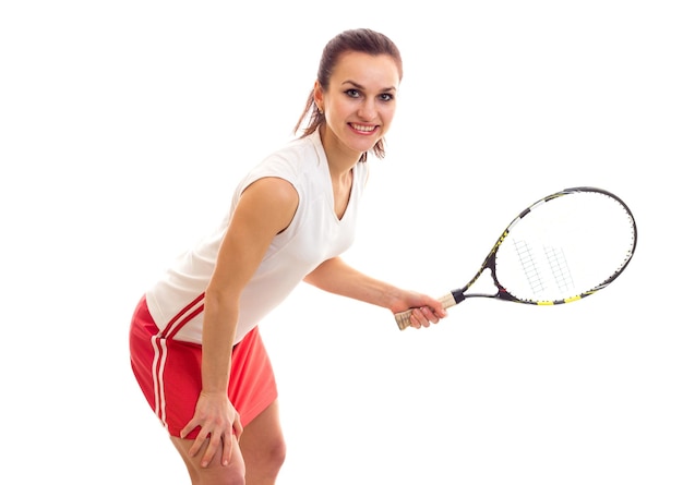 Jolie jeune femme en jupe rouge avec queue de cheval brune tenant une raquette de tennis et une balle jaune