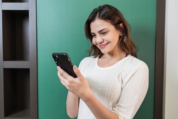 Jolie jeune femme latine à l'aide de smartphone debout sur fond blanc isolé se sentant heureux.