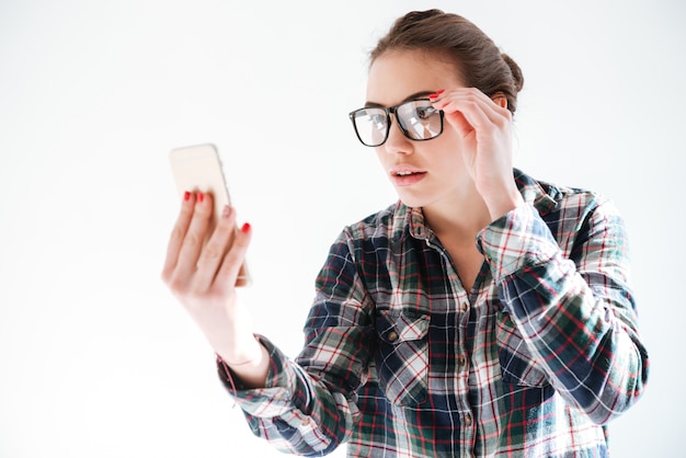 Jolie jeune femme à lunettes tenant et utilisant un téléphone portable