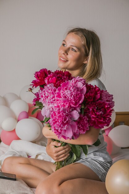 Jolie jeune femme à la maison dans la chambre au lit tenant des fleurs prendre un selfie par téléphone portable