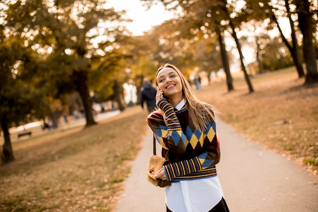 Jolie jeune femme marchant dans un parc en automne et utilisant un téléphone portable