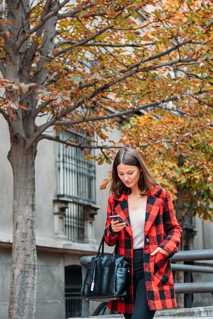 Jolie jeune femme marchant dans la rue à l'aide de téléphone