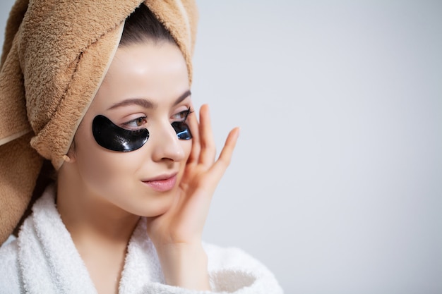 Jolie jeune femme met des patchs sous les yeux dans la salle de bain