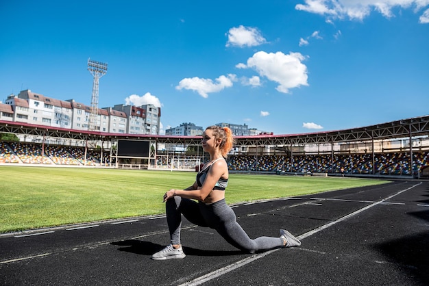 Jolie jeune femme mince en tenue de sport faisant des étirements dans le stade avant la journée de travail