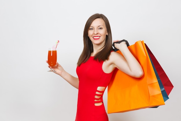 Jolie jeune femme à la mode glamour en robe rouge tenant un verre de cocktail à boire, des paquets multicolores avec des achats après le shopping isolés sur fond blanc. Copiez l'espace pour la publicité.