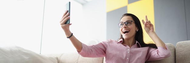 Jolie jeune femme montre un signe de paix et prend un selfie sur un smartphone