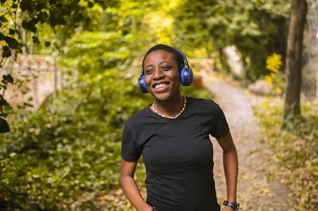 Jolie jeune femme noire africaine aux cheveux courts de beauté naturelle souriante et souriante avec des écouteurs bleus