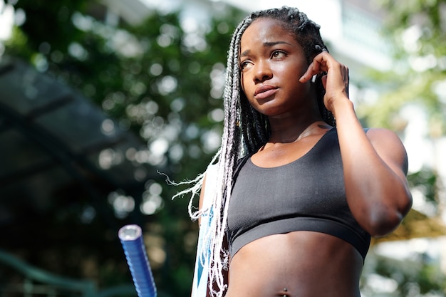 Jolie jeune femme noire écoutant de la musique dans les écouteurs en marchant vers un terrain de badminton avec une raquette à la main