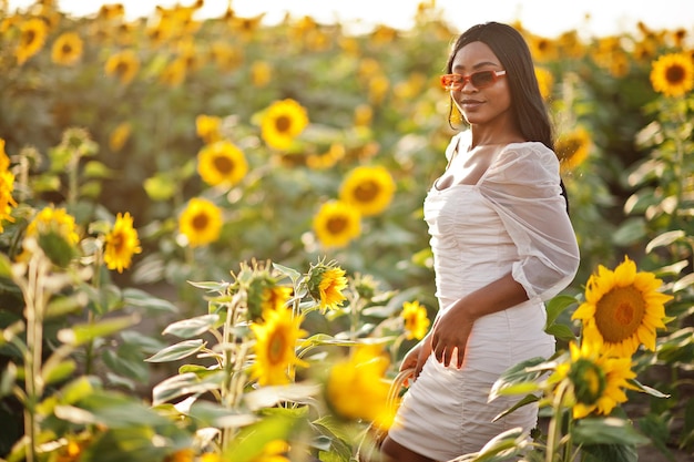 Jolie jeune femme noire porte une robe d'été pose dans un champ de tournesols.