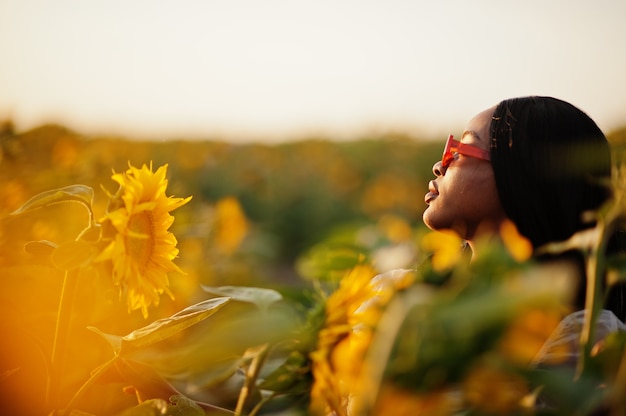 Jolie jeune femme noire vêtue d'une robe d'été pose dans un champ de tournesol.