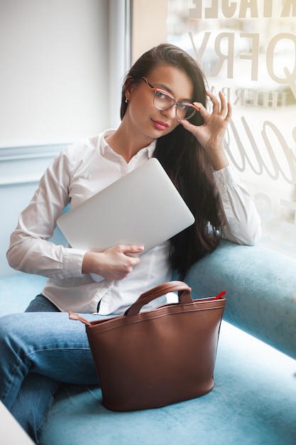 Jolie jeune femme avec ordinateur portable Femme à la cafétéria avec gadgets Femme d'affaires à l'intérieur