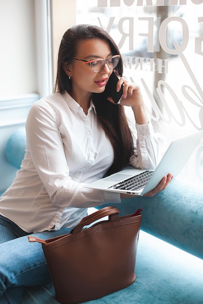 Jolie jeune femme avec ordinateur portable Femme à la cafétéria avec gadgets Femme d'affaires à l'intérieur