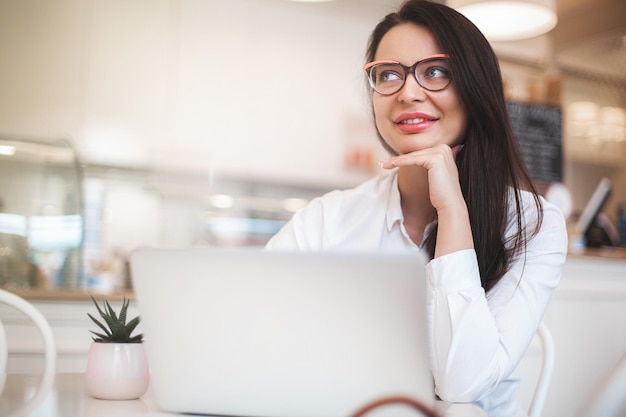 Jolie jeune femme avec ordinateur portable Femme à la cafétéria avec gadgets Femme d'affaires à l'intérieur