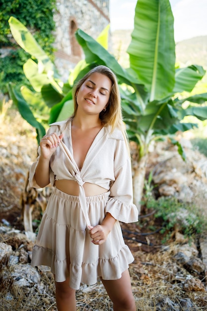 Jolie jeune femme à la peau claire se tient près des bananiers dans un parc tropical