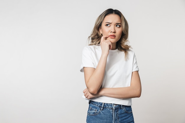 Une jolie jeune femme pensante posant isolée sur un mur blanc