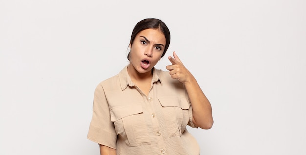 Jolie jeune femme pointant avec une expression agressive en colère ressemblant à un patron furieux et fou