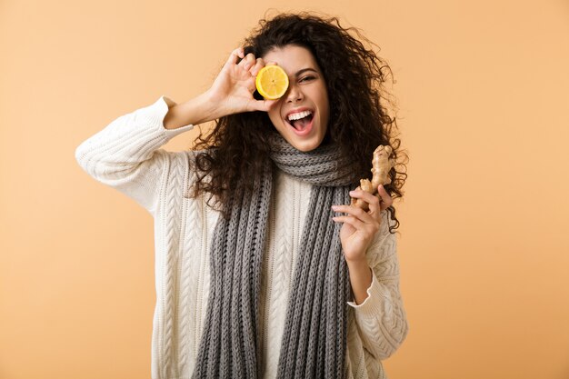 Jolie jeune femme portant un foulard d'hiver montrant le gingembre et le citron en position debout isolé sur un mur blanc