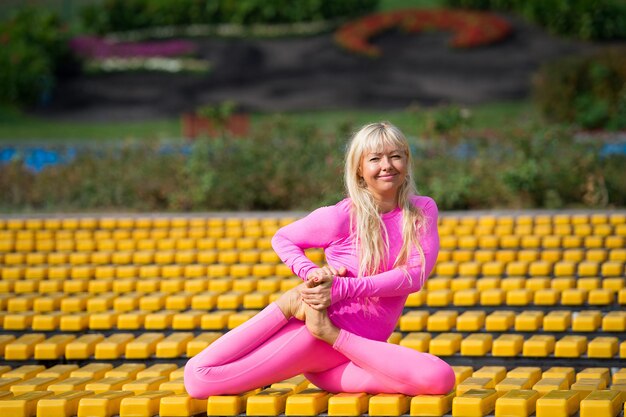 Jolie jeune femme portant des vêtements de sport roses faisant des asanas de yoga dans le parc à une journée ensoleillée sur fond jaune