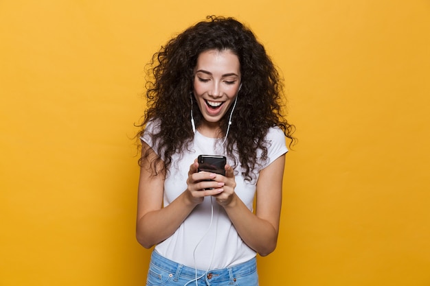 Jolie jeune femme posant isolée sur jaune à l'aide de musique d'écoute de téléphone portable.