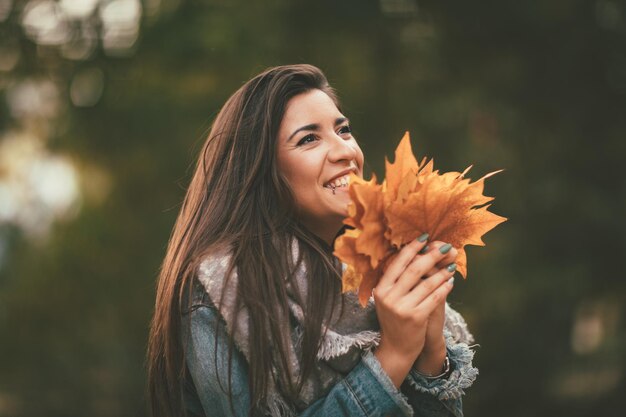 Jolie jeune femme profitant d'une forêt ensoleillée aux couleurs de l'automne. Elle tient des feuilles jaune d'or.