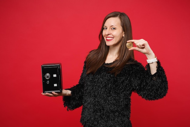 Jolie jeune femme en pull de fourrure tenant une banque de métal en toute sécurité pour l'accumulation d'argent monnaie future bitcoin isolée sur fond rouge. Les gens émotions sincères, concept de style de vie. Maquette de l'espace de copie.