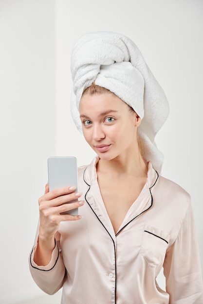 Jolie jeune femme en pyjama de soie va faire selfie tout en tenant le smartphone en face d'elle