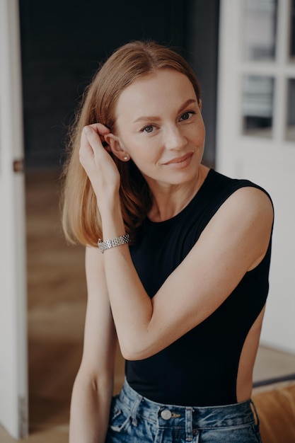 Jolie jeune femme de race blanche portant des vêtements décontractés fixant ses cheveux en regardant la caméra