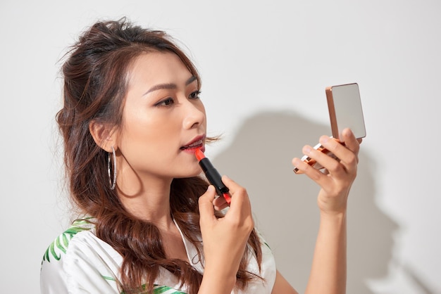 Jolie jeune femme rafraîchissant son rouge à lèvres de maquillage en tenant une boîte de poudre miroir de poche sur une journée ensoleillée