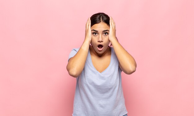 Jolie jeune femme à la recherche désagréablement choquée, effrayée ou inquiète, bouche grande ouverte et couvrant les deux oreilles avec les mains