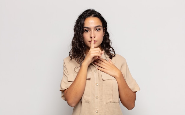 Jolie jeune femme à la recherche sérieuse et croisée avec le doigt appuyé sur les lèvres exigeant le silence ou le calme, gardant un secret