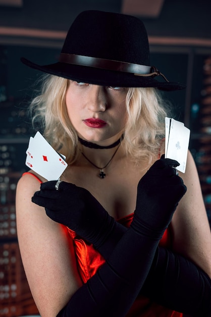 Jolie jeune femme en robe rouge et chapeau tenant une carte de poker as au casino