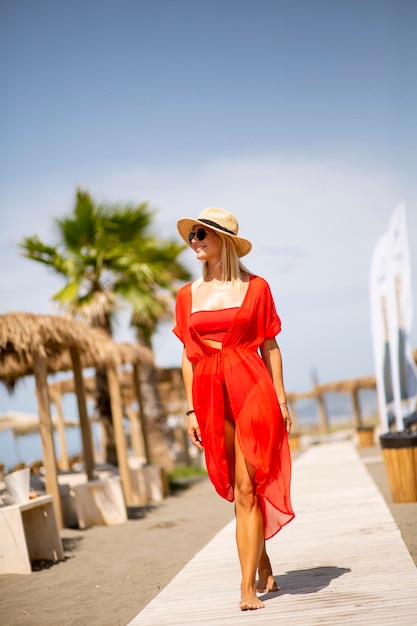 Jolie jeune femme en robe rouge marchant sur une plage en été