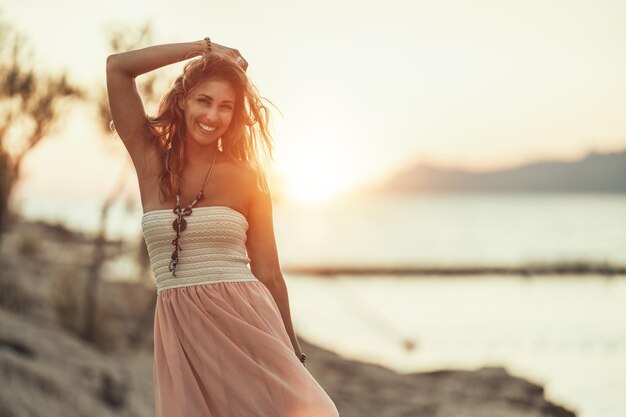 Une jolie jeune femme en robe s'amuse et profite du coucher de soleil d'été au bord de la mer magnifique.