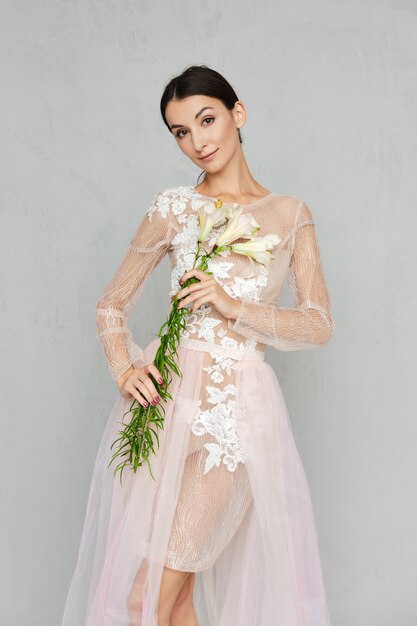 Jolie jeune femme en robe de tulle transparent avec dentelle posant avec des fleurs à la main