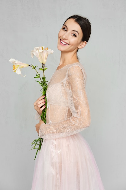 Jolie jeune femme en robe de tulle transparent avec dentelle posant avec des fleurs à la main