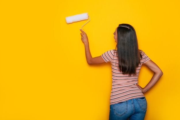 Jolie jeune femme avec un rouleau à peinture tout en travaillant pendant la rénovation de l'appartement