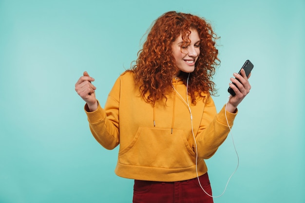 une jolie jeune femme rousse isolée, écoutant de la musique avec des écouteurs