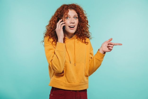 Une jolie jeune femme rousse isolée, parlant au téléphone portable, riant