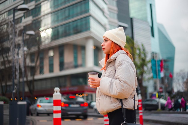 Jolie jeune femme rousse à la mode élégante marchant et traversant la route dans une ville moderne