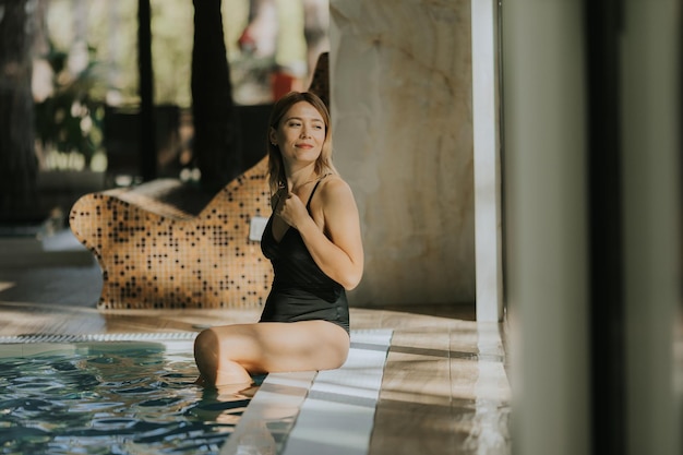 Une jolie jeune femme se détend au bord de la piscine intérieure.