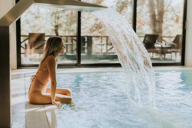 Jolie jeune femme se relaxant au bord de la piscine intérieure