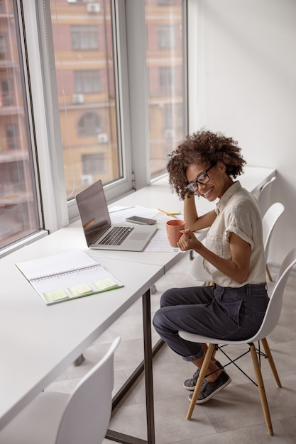 Jolie jeune femme se reposant tout en tenant une tasse de boisson au bureau