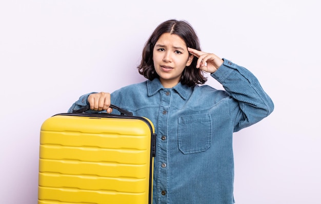 Jolie jeune femme se sentant confuse et perplexe, vous montrant que vous êtes fou. concept de valise de voyage