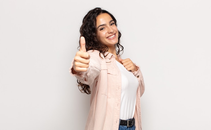 Photo jolie jeune femme se sentant fière, insouciante, confiante et heureuse, souriant positivement avec le pouce levé