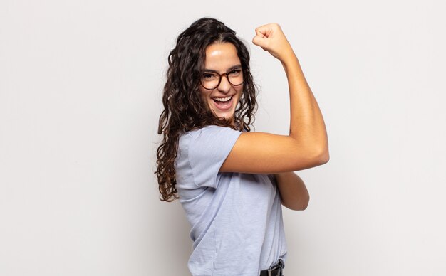 Jolie jeune femme se sentant heureuse, satisfaite et puissante, ajustement flexible et biceps musclé, regardant fort après la salle de gym