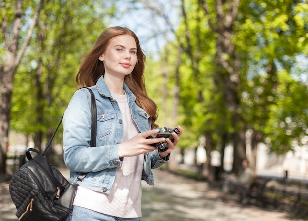 Jolie jeune femme séduisante touriste en veste en jean avec appareil photo rétro dans la ville